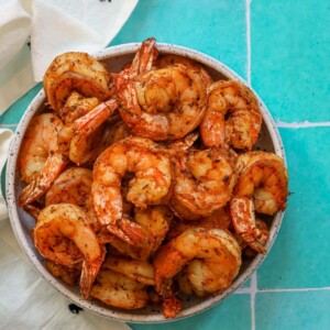 Grilled blackened shrimp in a bowl on a blue tile.