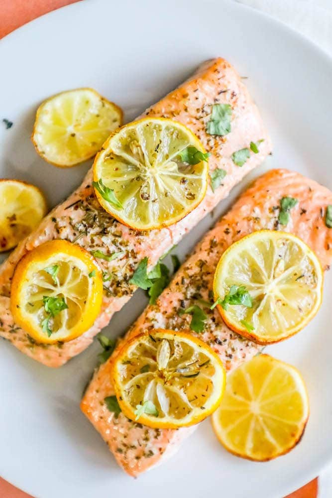 salmon filets with lemon slices, garlic and herbs on top on a white plate