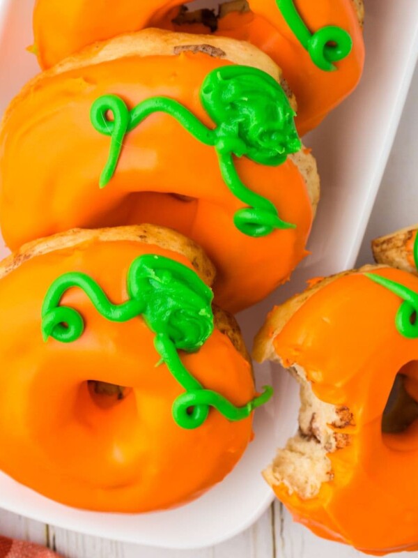 air fried pumpkin donuts with orange frosting and green pumpkin stem icing on top on a plate