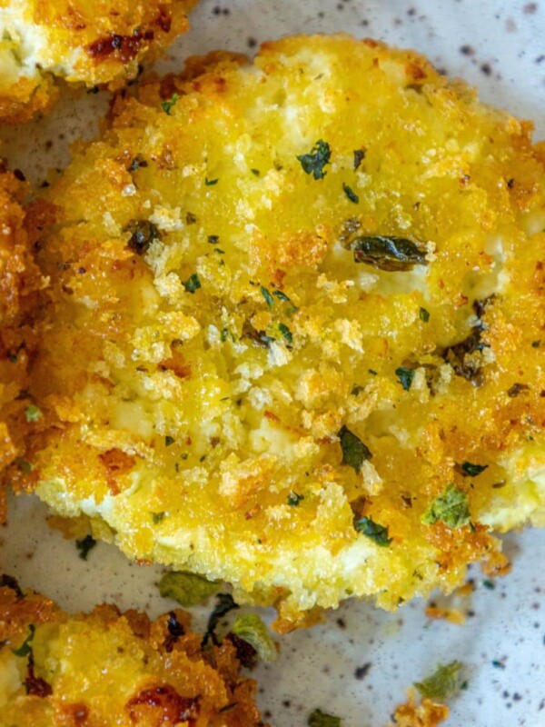 golden baked panko covered goat cheese balls on a white speckled plate and topped with dried herbs