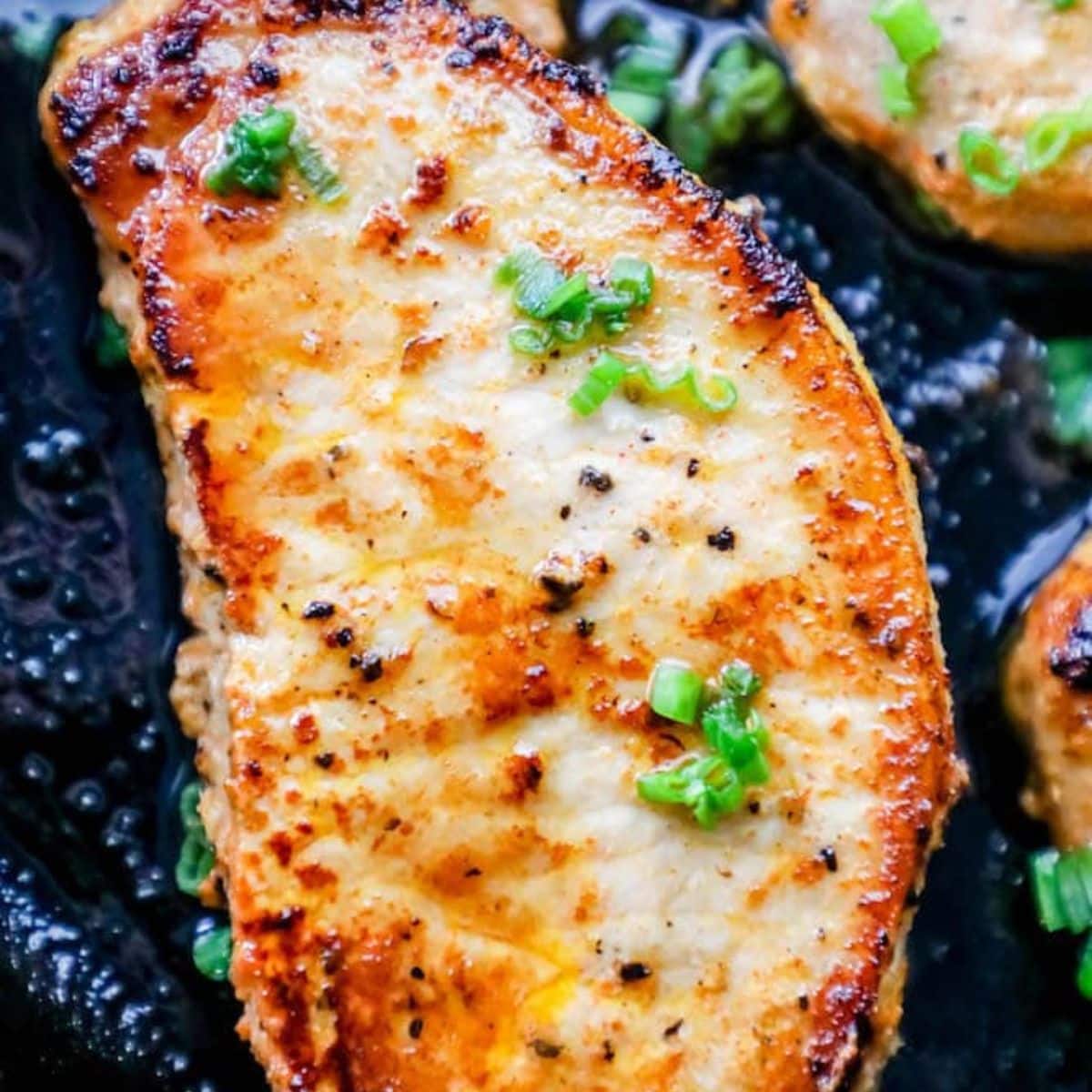 a baked pork chop in a cast iron pan with chives on top