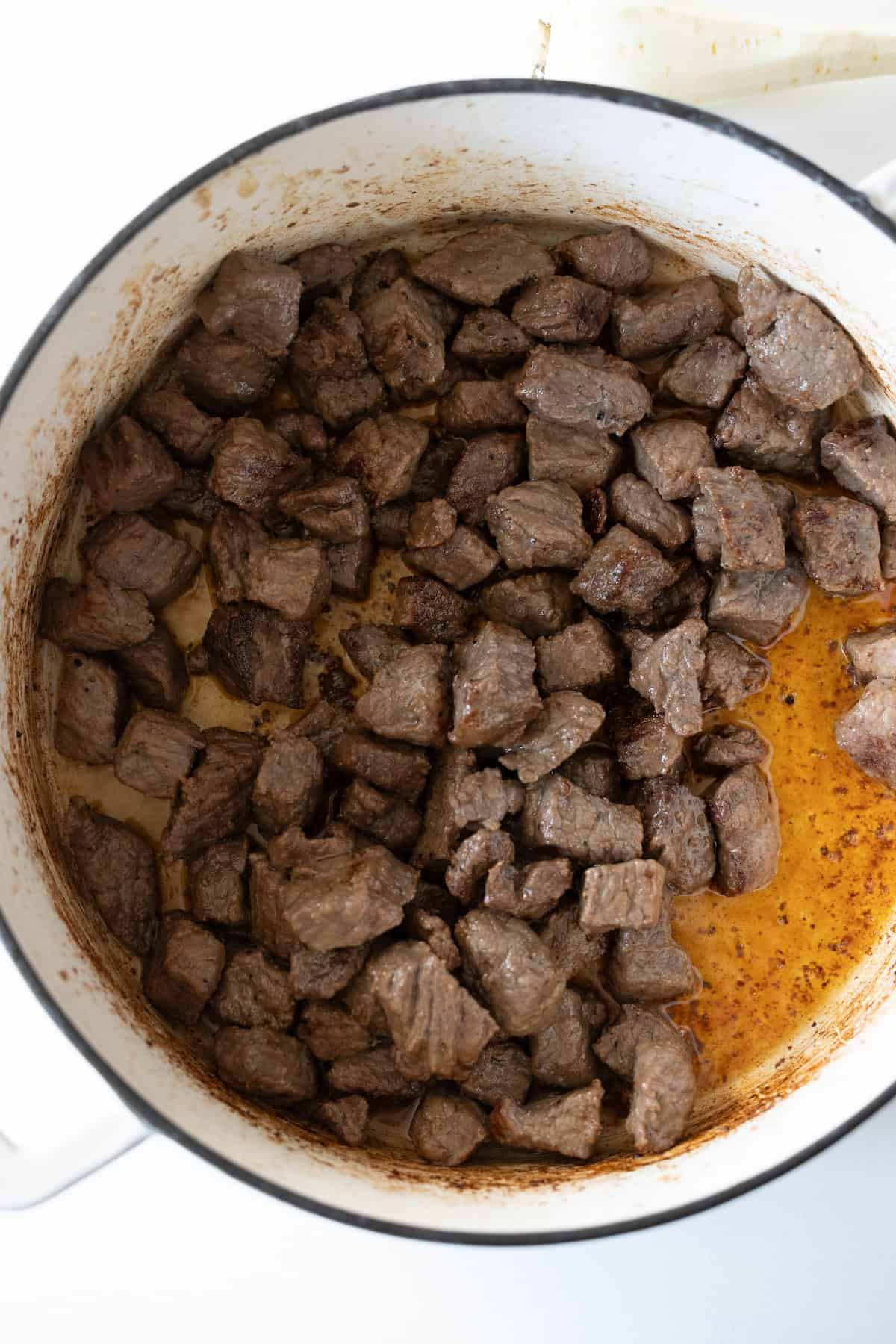 Cooked beef cubes in a white pot, with browned edges and some savory cooking juices mingling at the bottom—a perfect start for a hearty beef stew.