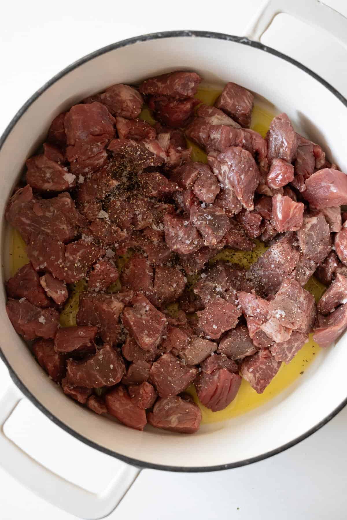 Chunks of raw beef and parsnip, seasoned with salt and pepper, sizzle in a white pot with olive oil.