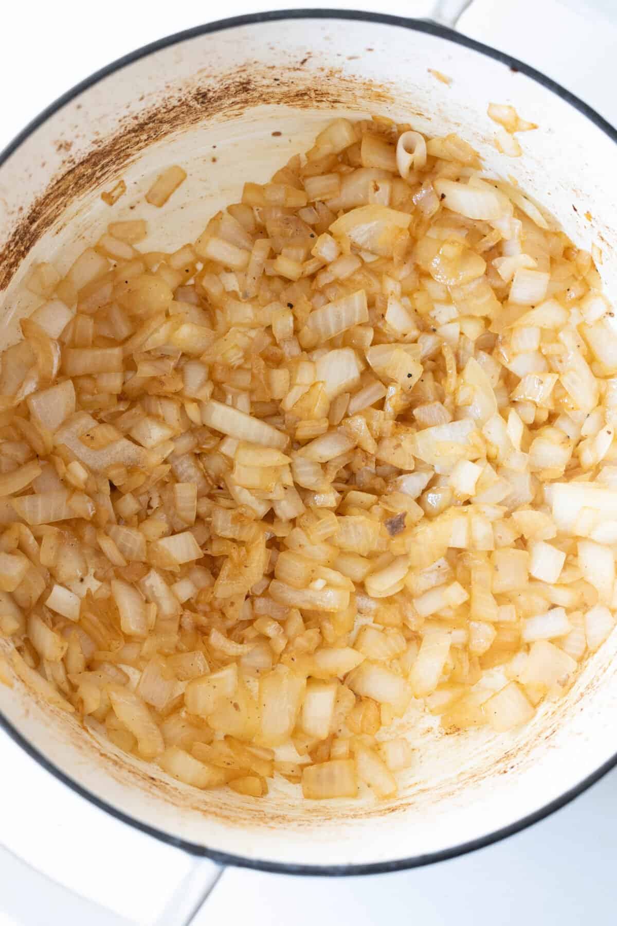 Chopped onions are being sautéed in a pot, slightly browned and translucent, forming the aromatic base for a hearty beef stew.