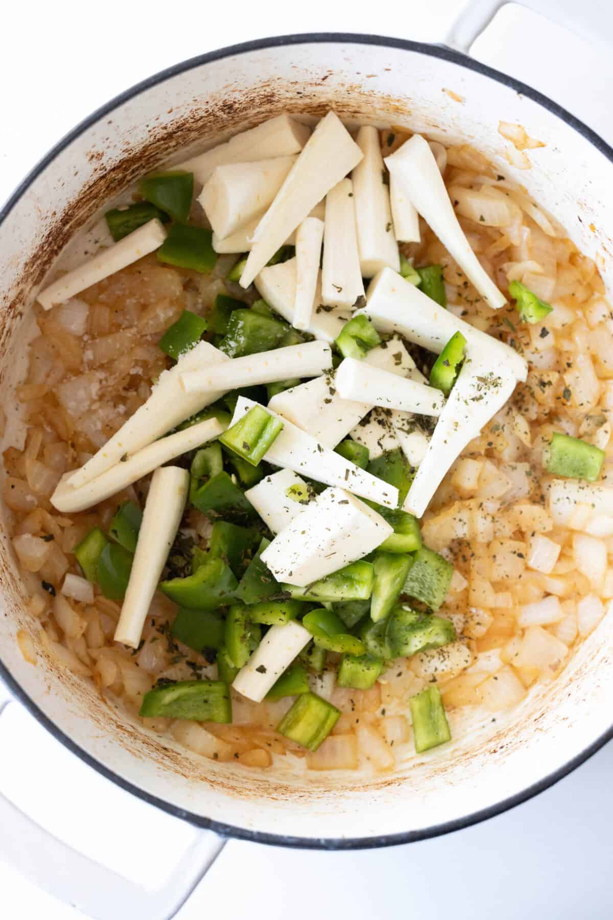 Chopped onions, green bell peppers, and parsnips are simmering in a pot of savory beef stew.