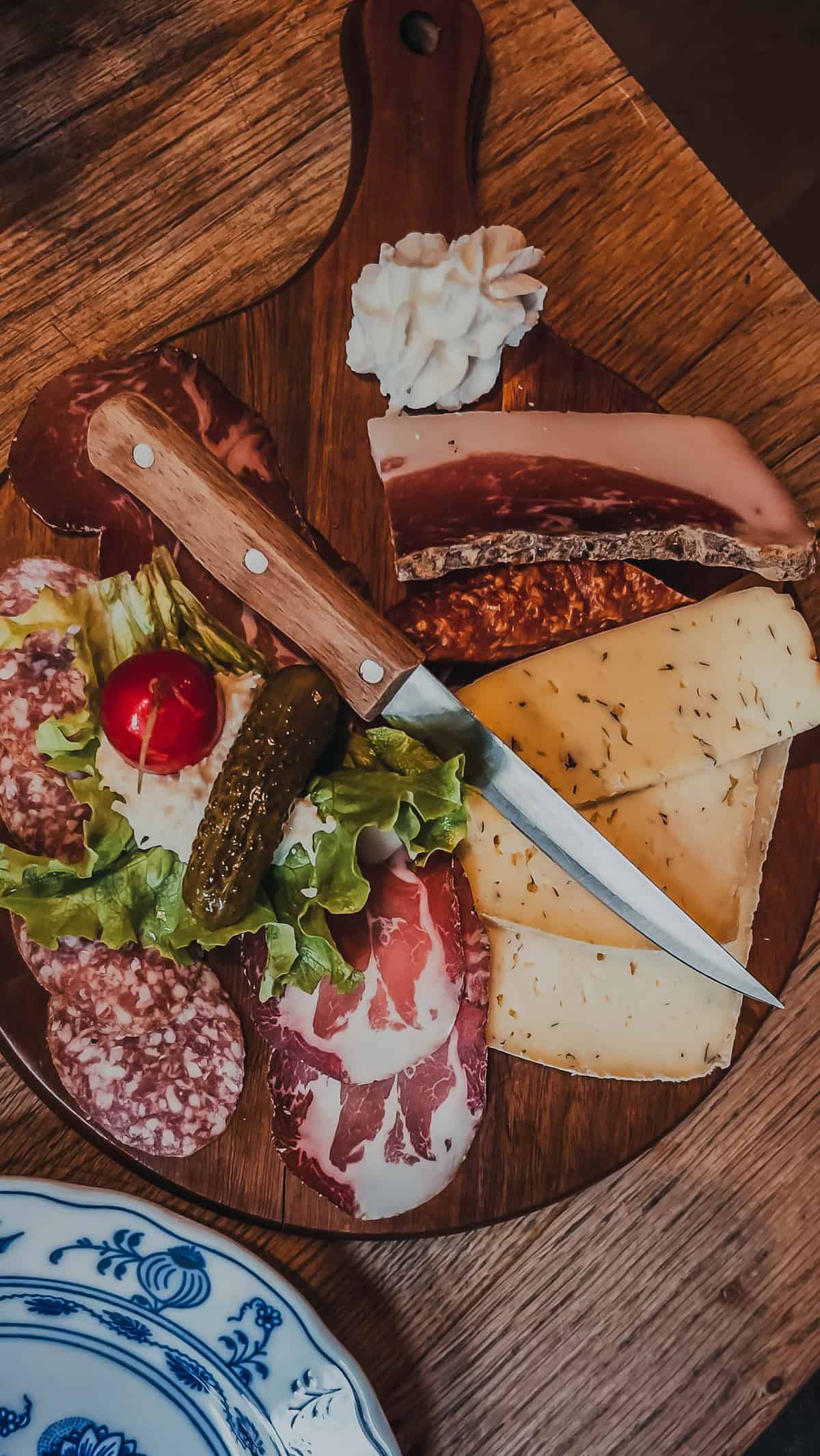 A wooden board at the Bolzano market, adorned with assorted meats, cheeses, lettuce, a pickle, a cherry tomato, and a dollop of cream, invites indulgence. A perfect festive delight to savor with a knife in hand during the Christmas season.