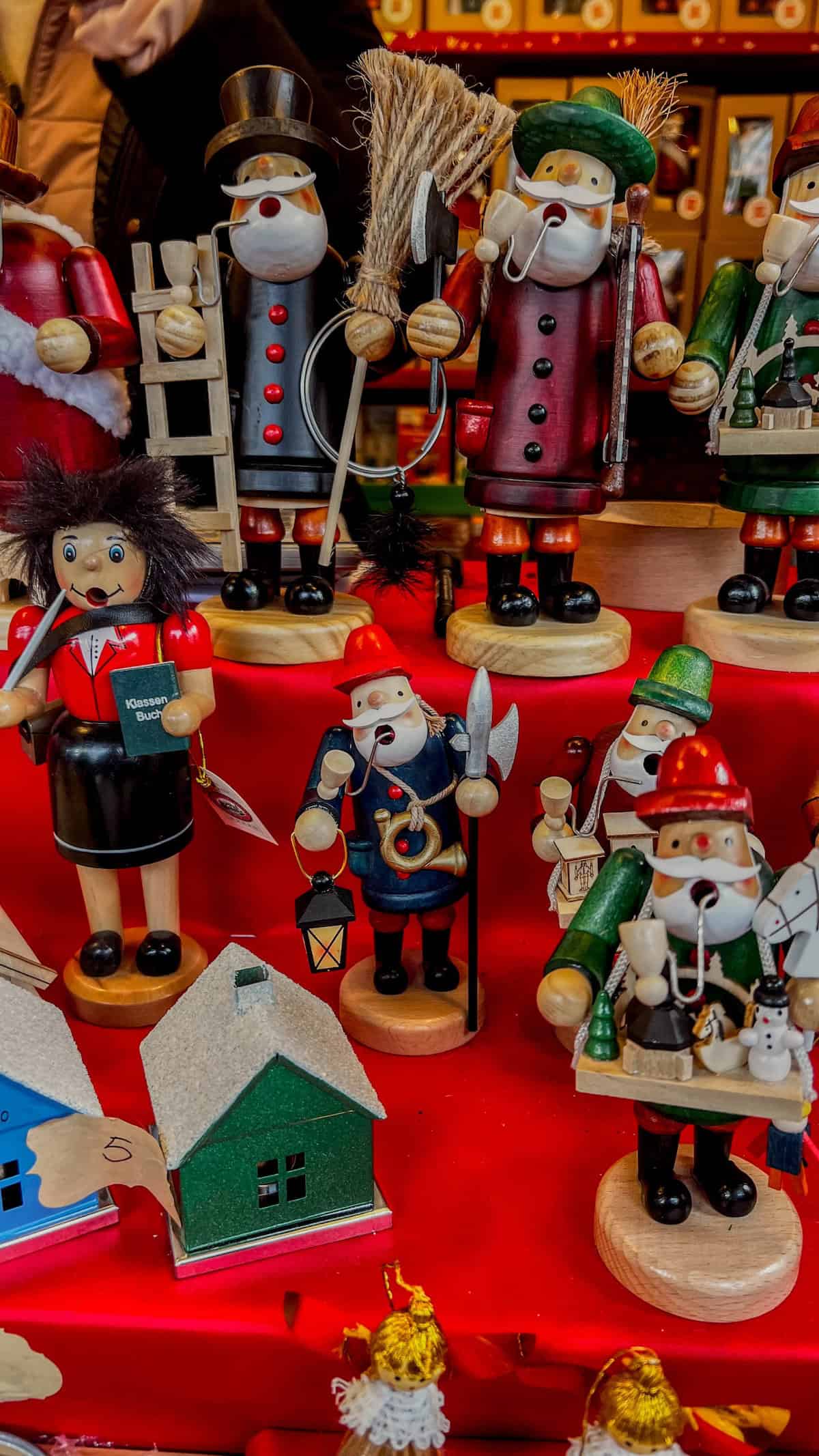 A festive display features wooden nutcracker figures in various costumes, arranged on a red surface. In front, small green and gray model houses evoke the charm of Bolzano's Christmas market.