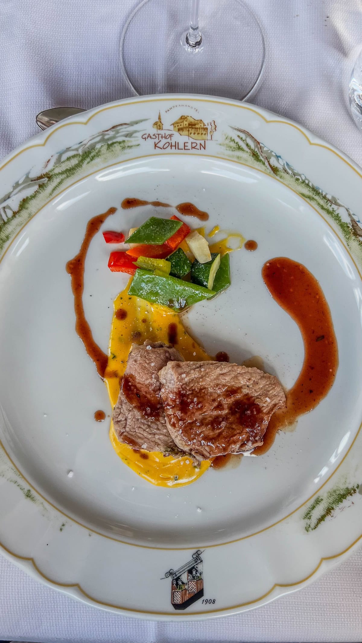 A plated dish with sliced meat and sauce, accompanied by colorful vegetables, garnished with a drizzle of sauce on a decorative plate that evokes the festive charm of the Bolzano Christmas Market.