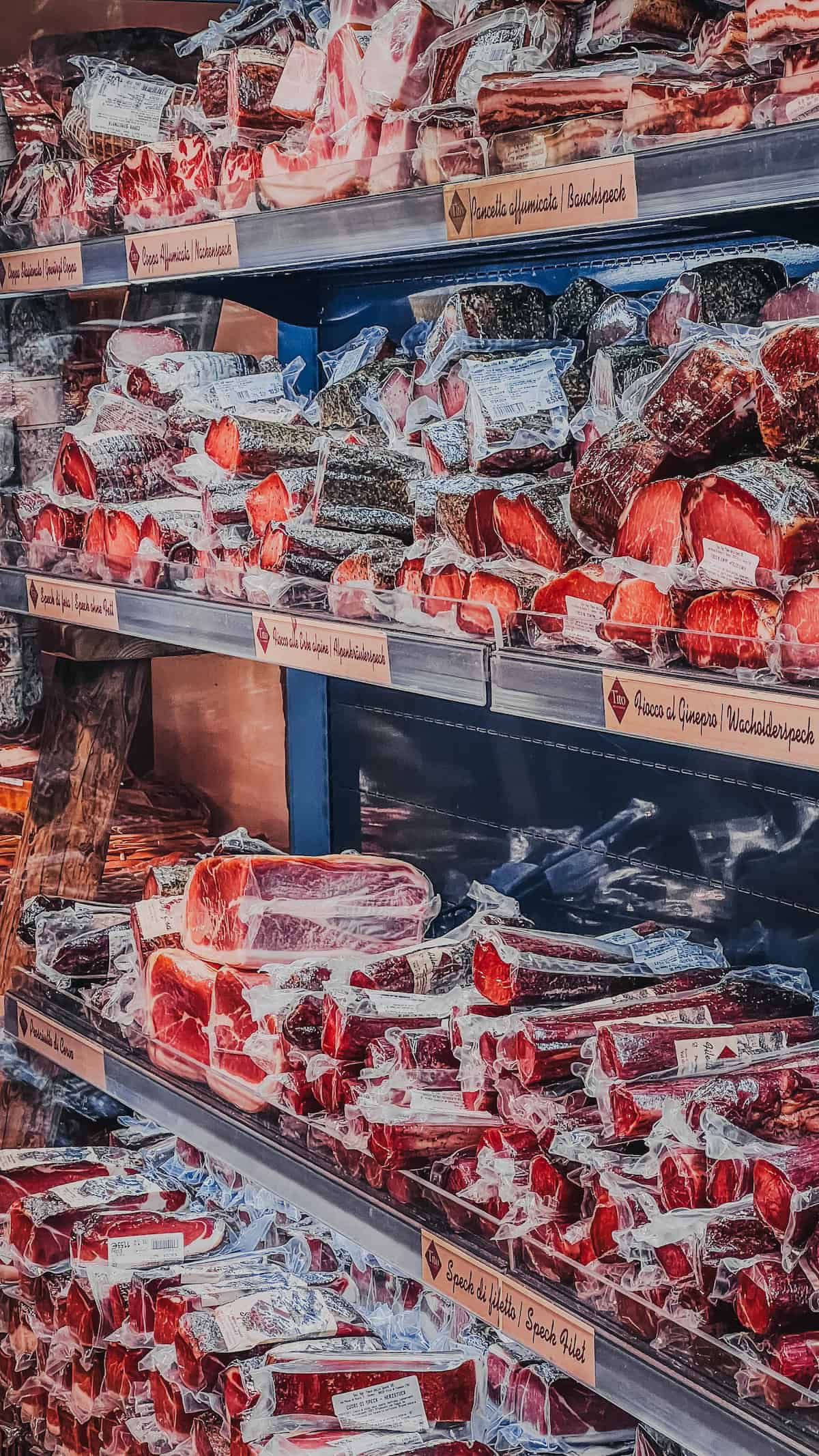 Shelves in Bolzano's market are stocked with various vacuum-sealed cured meats and sausages in a festive display, perfect for Christmas shopping.