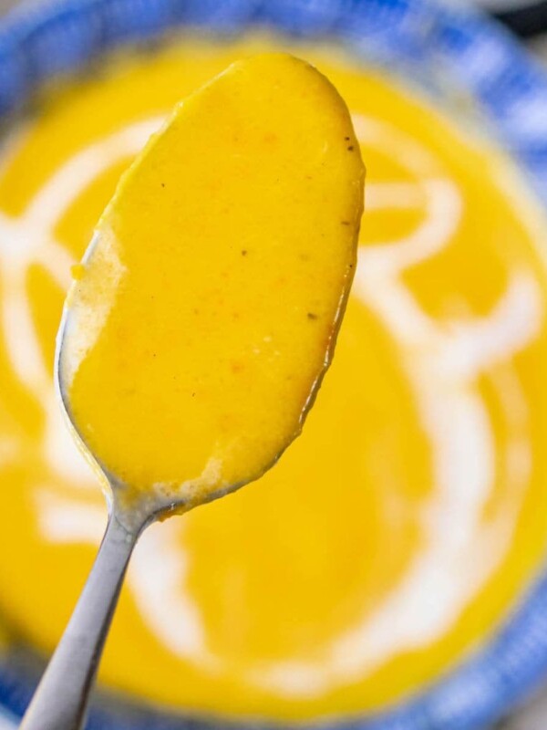 A spoon is holding a bowl of butternut squash soup.