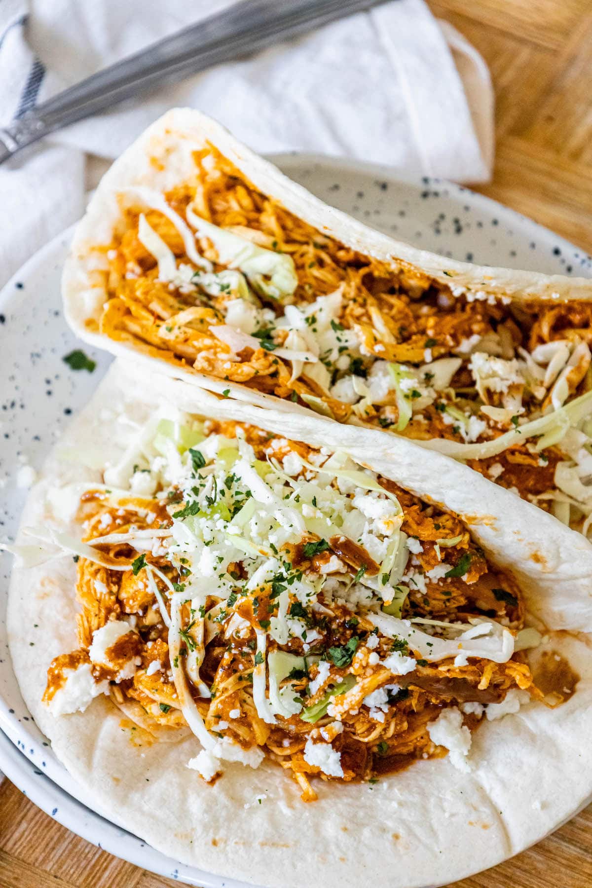 shredded chicken tinga in a tortilla with chopped cilantro, cabbage, and crumbled cotija cheese on top