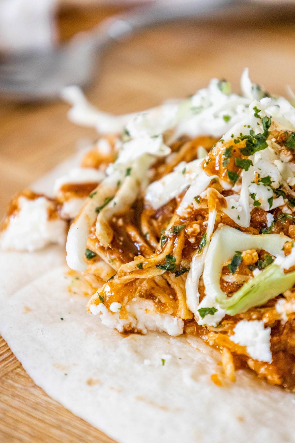 shredded chicken tinga in a tortilla with chopped cilantro, cabbage, and crumbled cotija cheese on top