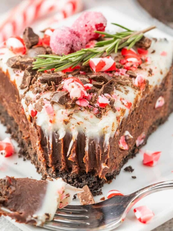 A slice of chocolate peppermint cheesecake with a candy cane garnish on a plate.