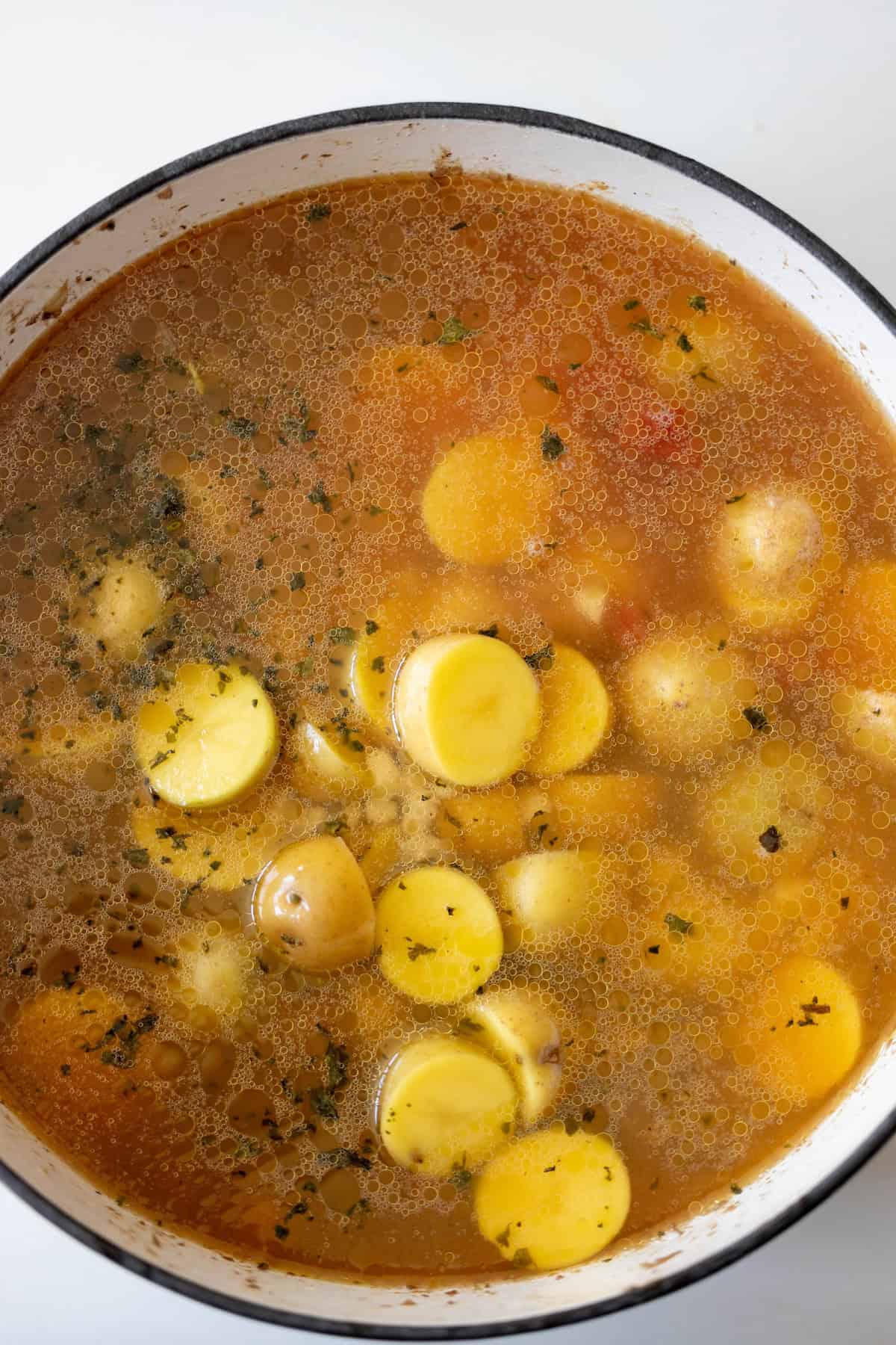 A close-up of a pot filled with a vegetable soup, showing potato slices, broth, and herbs reminiscent of a classic stew.