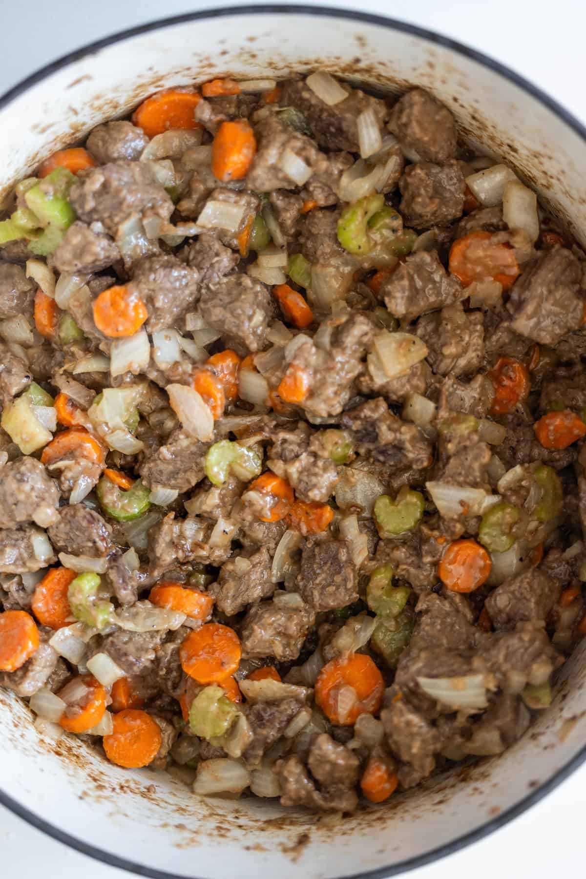 A close-up of a pot filled with a mixture of diced beef, carrots, celery, and onions, creating a classic beef stew.