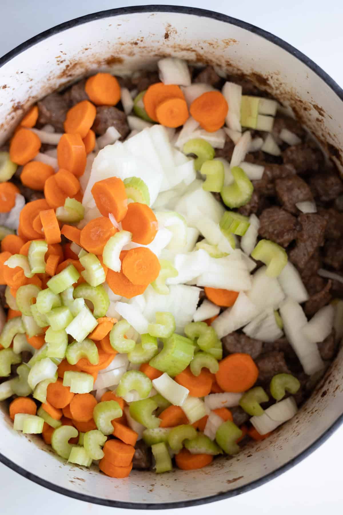 A pot filled with sliced carrots, celery, onions, and tender beef pieces is ready for further cooking into a hearty beef stew.