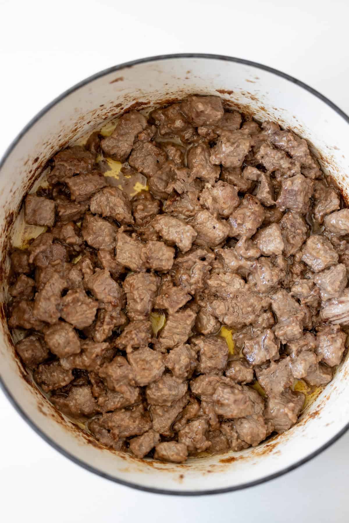 A pot filled with browned, cubed pieces of beef in a light sauce, perfect for a classic beef stew.