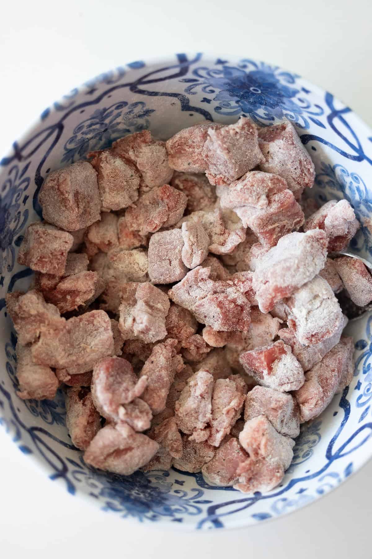 Chunks of raw meat coated in flour sit in a blue and white patterned bowl, ready to become a classic beef stew.