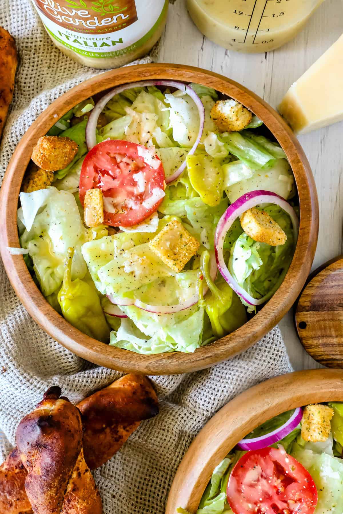 A bowl of salad containing lettuce, tomato slices, red onion rings, croutons, and a creamy dressing. A jar of vegan mayonnaise, a container of dressing, and breadsticks are visible around the bowl.