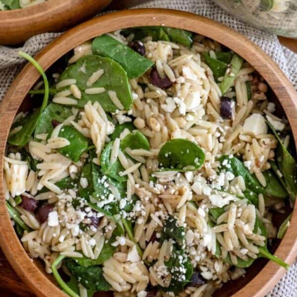 A wooden bowl filled with feta orzo salad recipe, featuring spinach, black olives, and crumbled feta cheese.