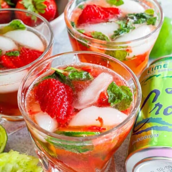 Three glasses of refreshing strawberry and mint mocktails with ice, accompanied by a can of LaCroix lime sparkling water, fresh strawberries, and a halved lime.