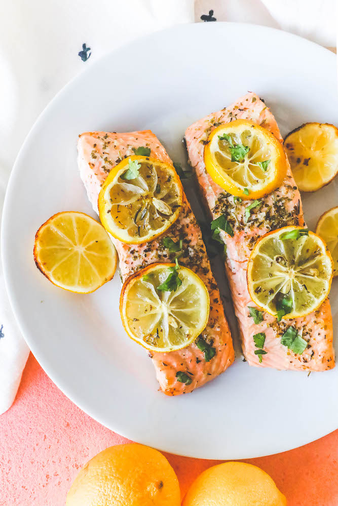 salmon filets with lemon slices, garlic and herbs on top on a white plate