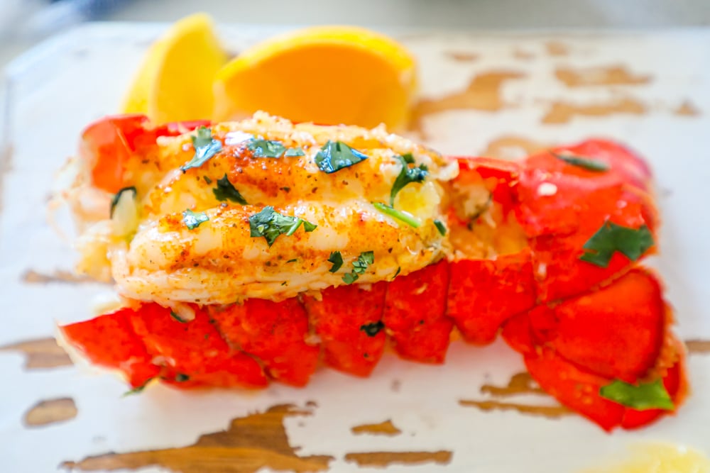 lobster tail on a white painted cutting board with parsley on top 