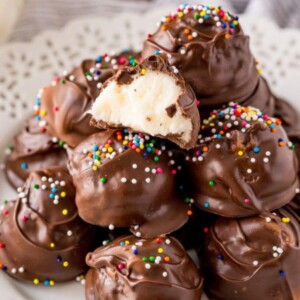 chocolate dipped buttercream candies on a white plate with rainbow sprinkles on top