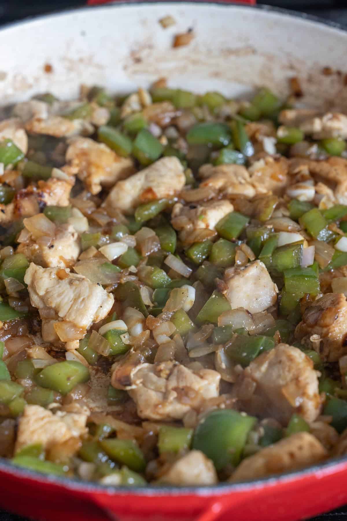 A close-up of a red skillet containing cooked chicken pieces, diced bell peppers, and chopped onions, perfect for a One Pan Chicken Risotto.