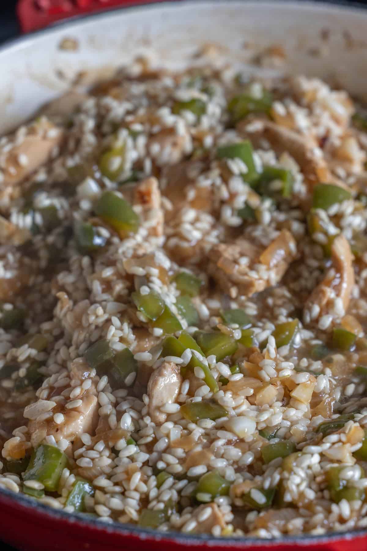 A close-up of a pan filled with a mixed dish containing rice, diced green bell peppers, and what appears to be pieces of chicken, all mixed together in a sauce. This One Pan Chicken Risotto showcases an easy, flavorful blend that simplifies how to cook risotto.