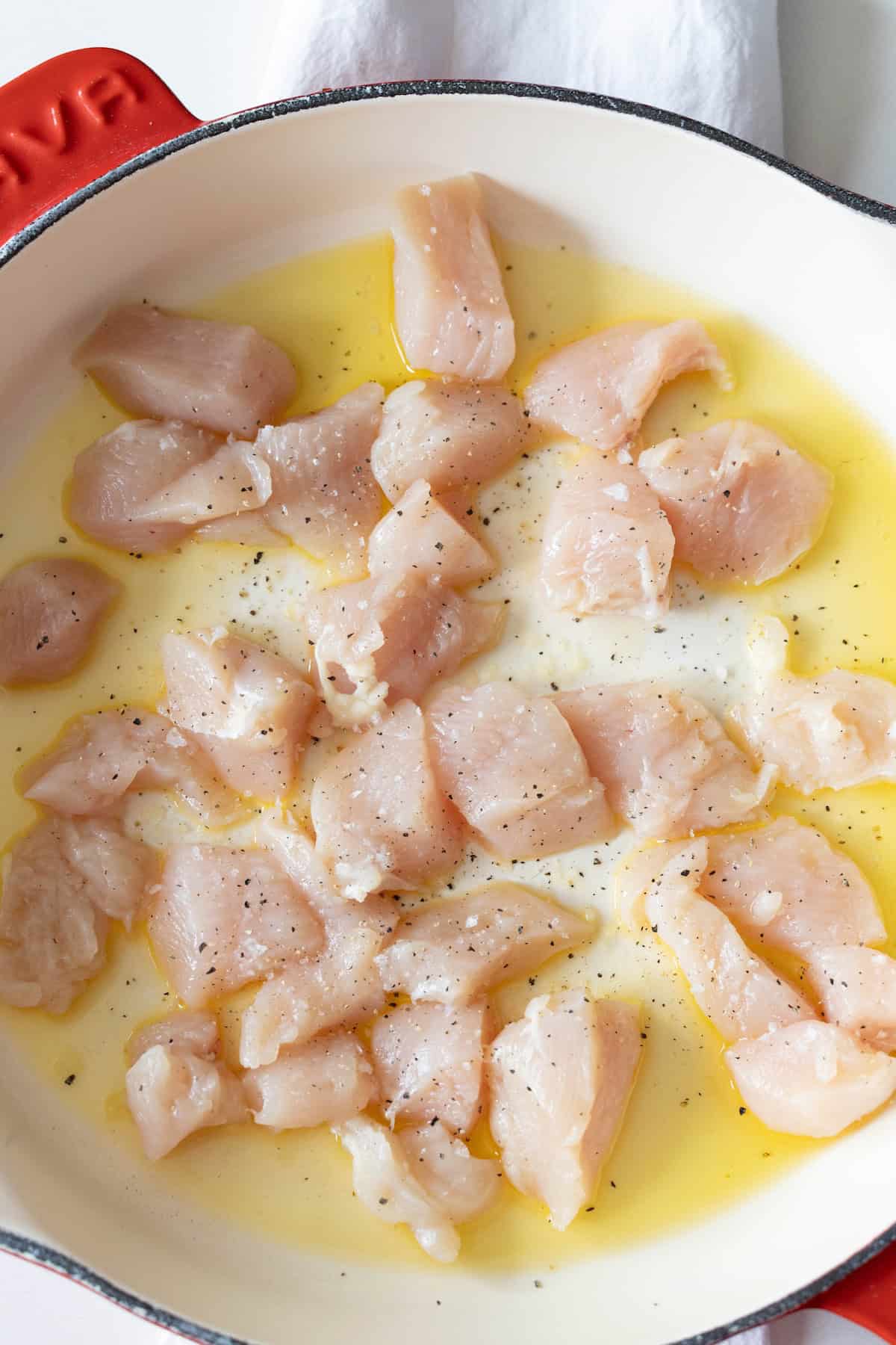 Diced raw chicken pieces seasoned with salt and pepper sizzle in a light-colored pan with oil, setting the stage for an easy one pan chicken risotto recipe.