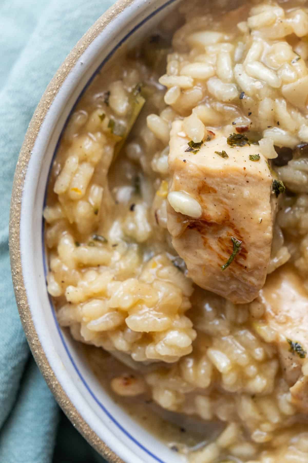 A close-up of a creamy chicken risotto dish, perfect for an easy risotto recipe, served in a white bowl on a light blue cloth.