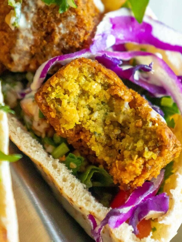 three pitas stuffed with falafel balls, cabbage, and salad with tahini sauce ladled on top