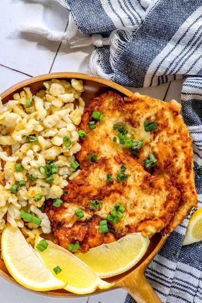 spaetzle and schnitzel in a wooden dish with a slice of lemon and sliced green onions on top