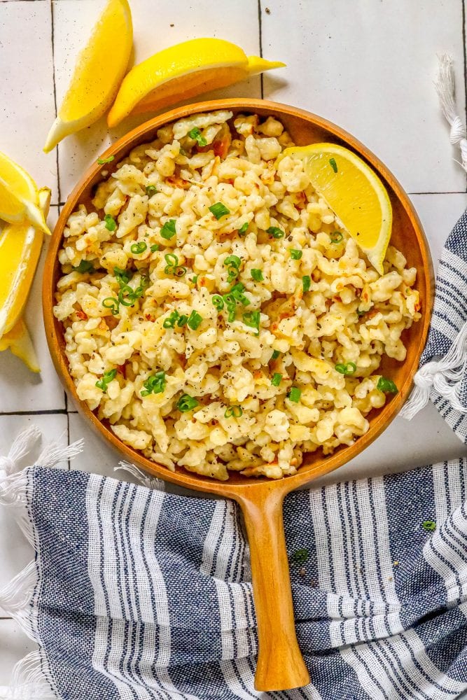 spaetzle in a wooden dish with a slice of lemon and sliced green onions on top