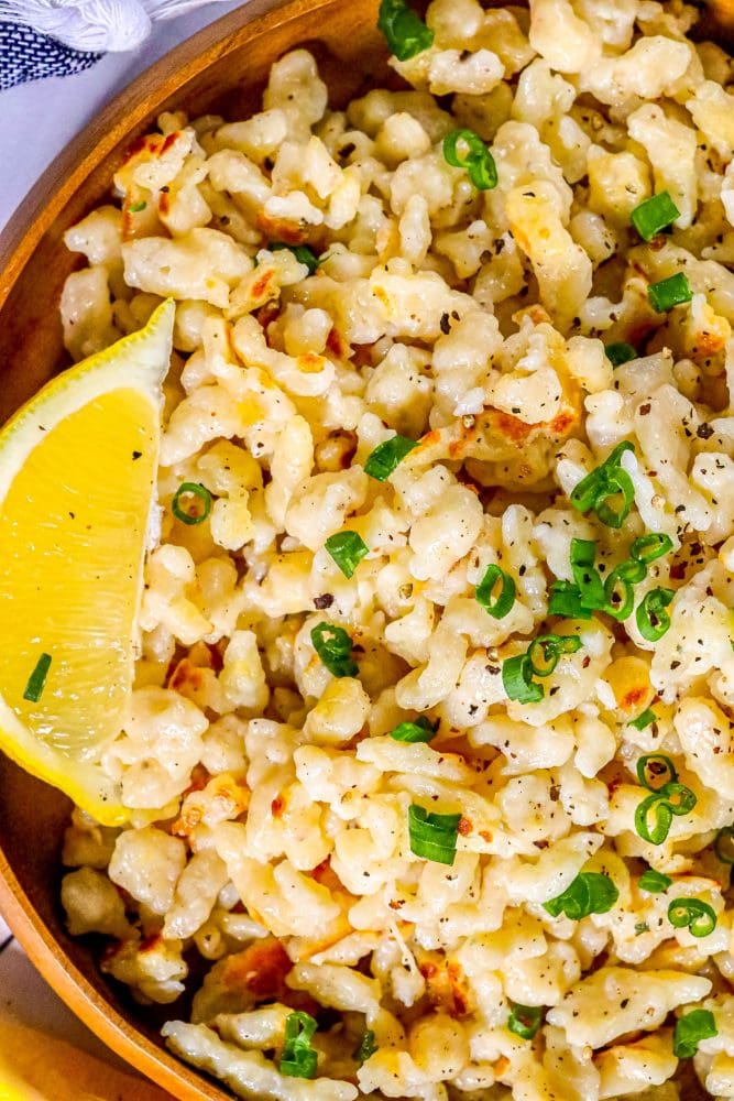 spaetzle in a wooden dish with a slice of lemon and sliced green onions on top