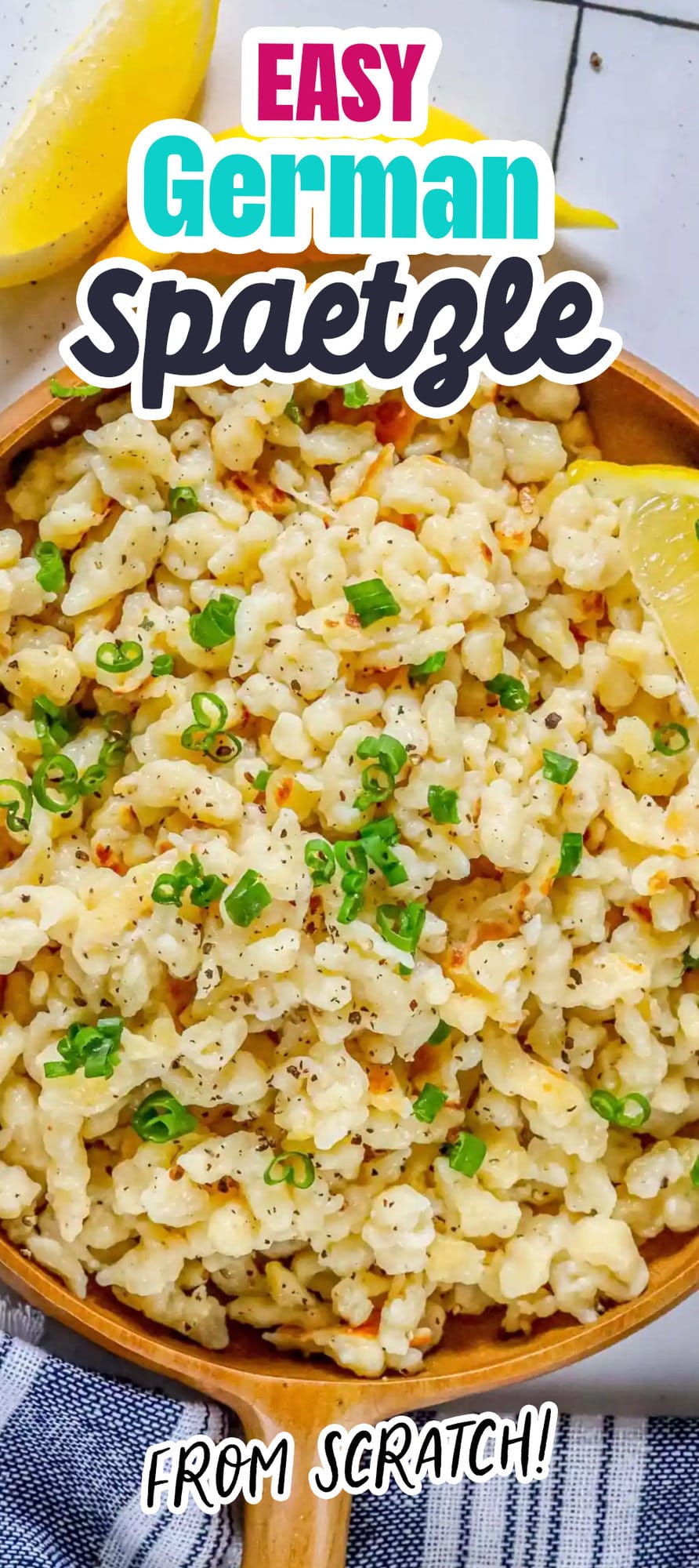 spaetzle noodles on a wooden plate with fresh pepper and sliced green onions on top next to a lemon wedge