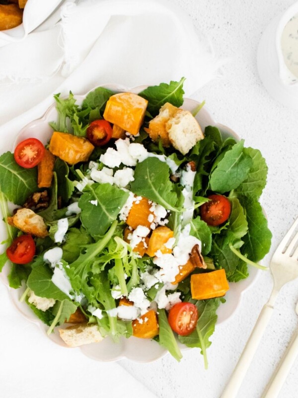 A plate with a Roasted Sweet Potato and Goat Cheese salad and dressing on it.