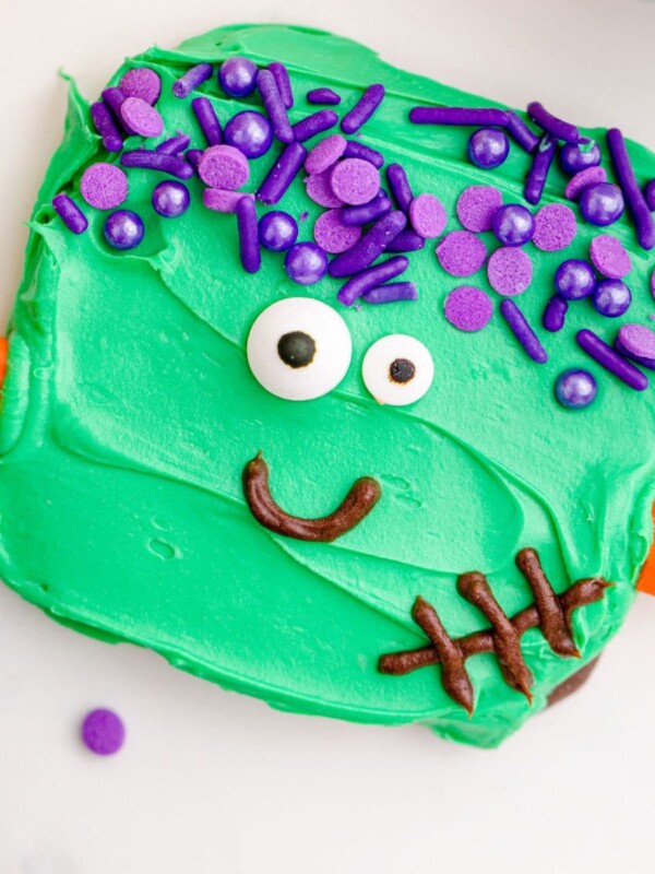 picture of chocolate dipped cookies, covered in green icing with purple sprinkles for hair, candy corn neck bolts, candy eyes, and an icing smile to look like frankenstein