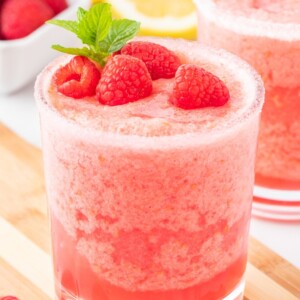 frozen pink lemonade in a sugar rimmed glass with raspberries and a sprig of mint on top