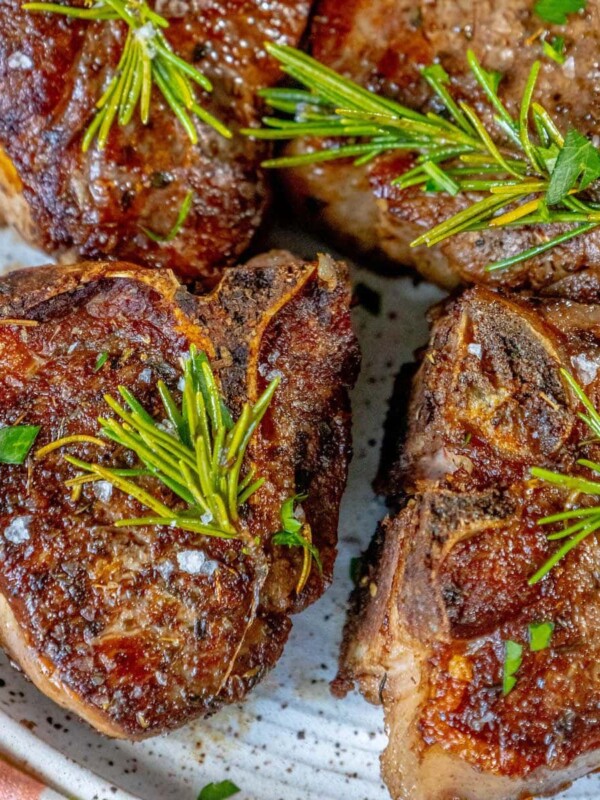 seared lamb chop on a white plate with a sprig of rosemary and sea salt flakes and a white wine shallot sauce on top