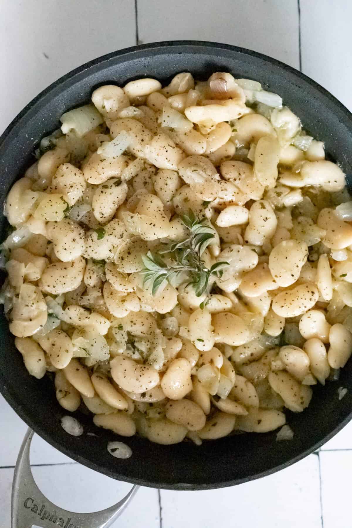 A pan filled with cooked butter beans, seasoned with pepper and topped with fresh herbs and a hint of garlic.