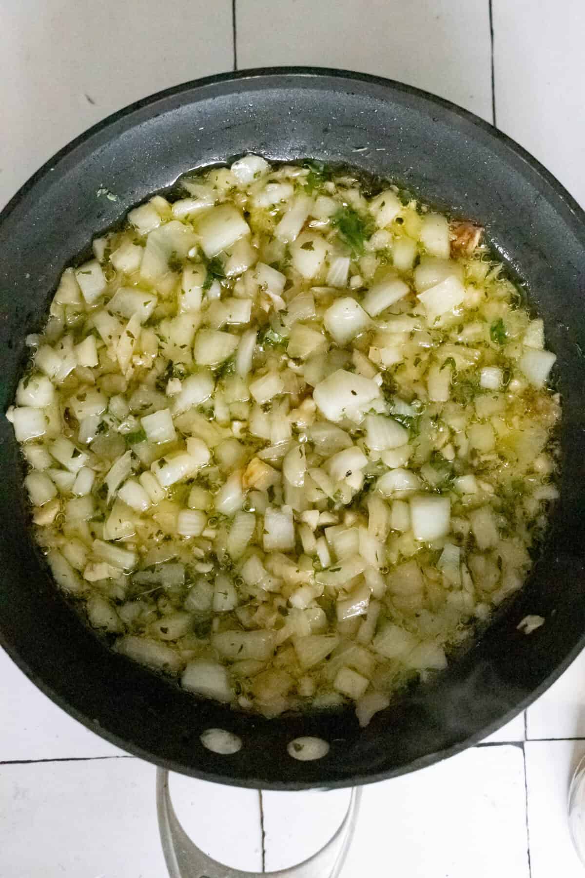 A pan with chopped onions and garlic sautéing in oil on a stove.