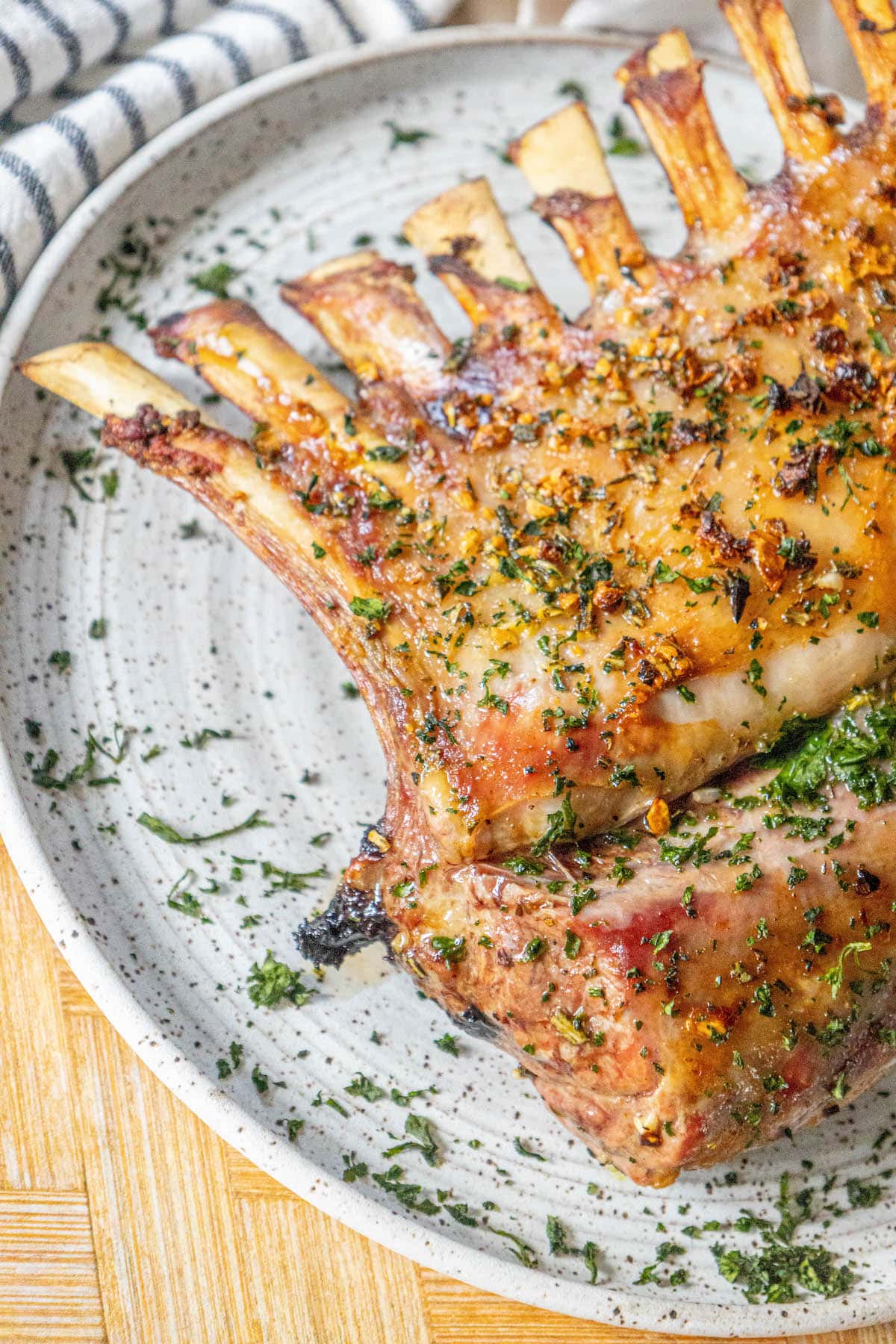 roasted rack of lamb with garlic and herb crust on a white speckled plate on a table