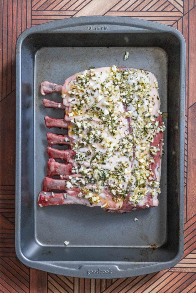 rack of lamb coated in herbs, olive oil, minced garlic in a roasting pan 