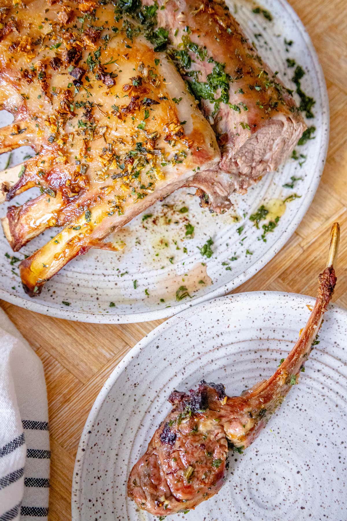 roasted rack of lamb with garlic and herb crust on a white speckled plate on a table