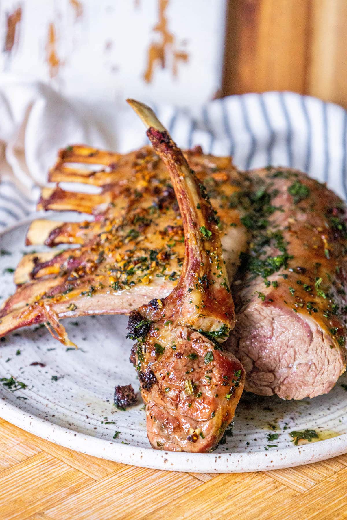 roasted rack of lamb with garlic and herb crust on a white speckled plate on a table