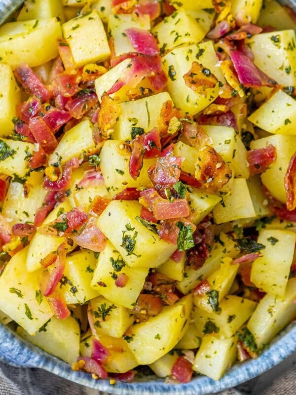 picture of german potato salad with red onions, herbs, and bacon on top in a blue bowl on a table