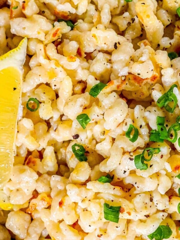 spaetzle noodles on a wooden plate with fresh pepper and sliced green onions on top next to a lemon wedge