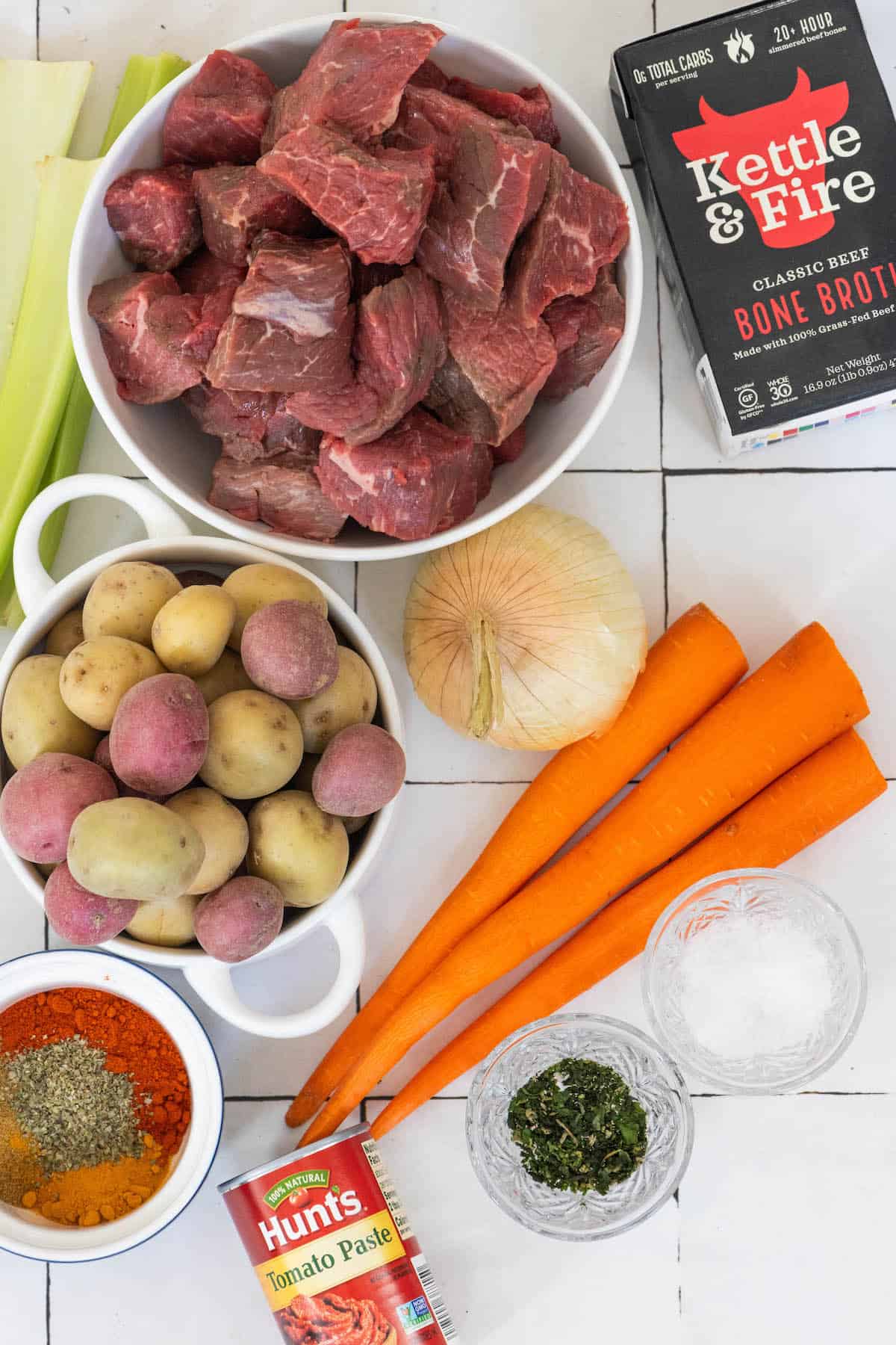 The ingredients for a goulash beef stew are laid out on a tiled floor.